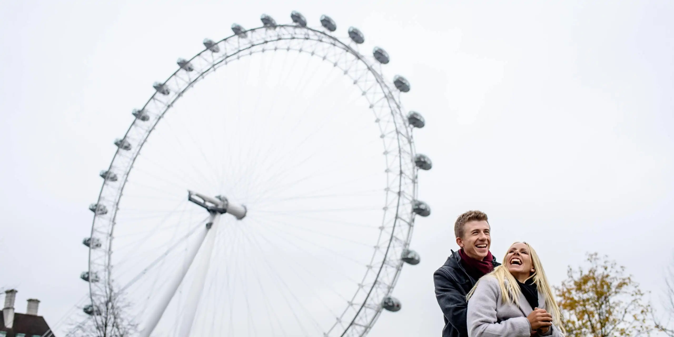 Laughing couple in front of the London Eye for their winter engagement photography session