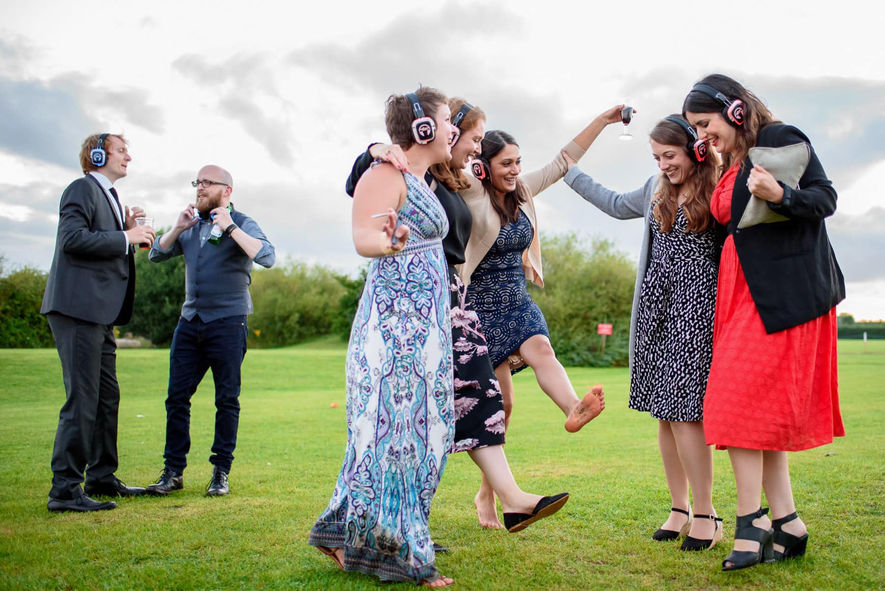 A group of wedding guests dancing outside in a field with silent disco headphones