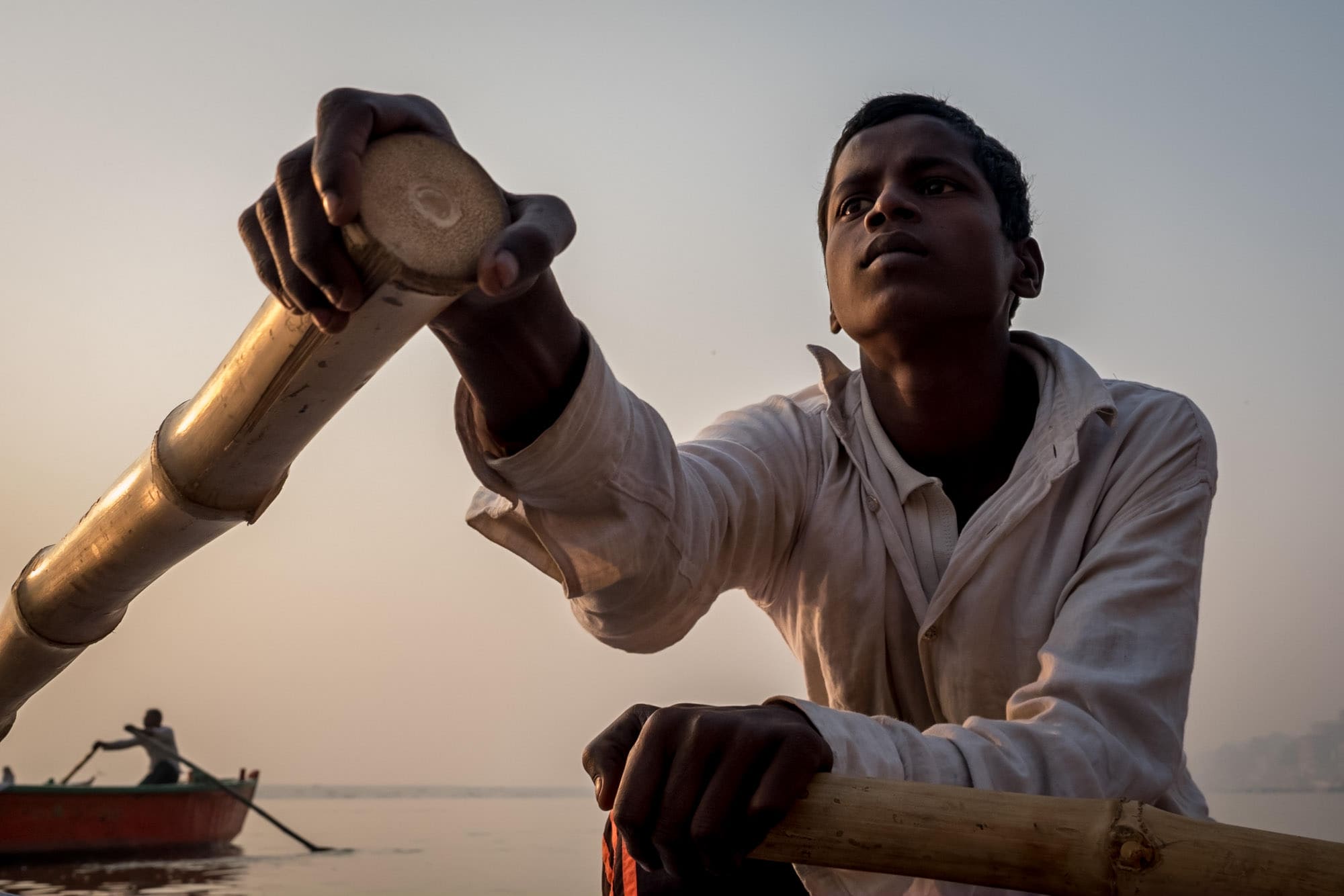 Boy rowing boat at sunrise on Ganges in Varanasi, India