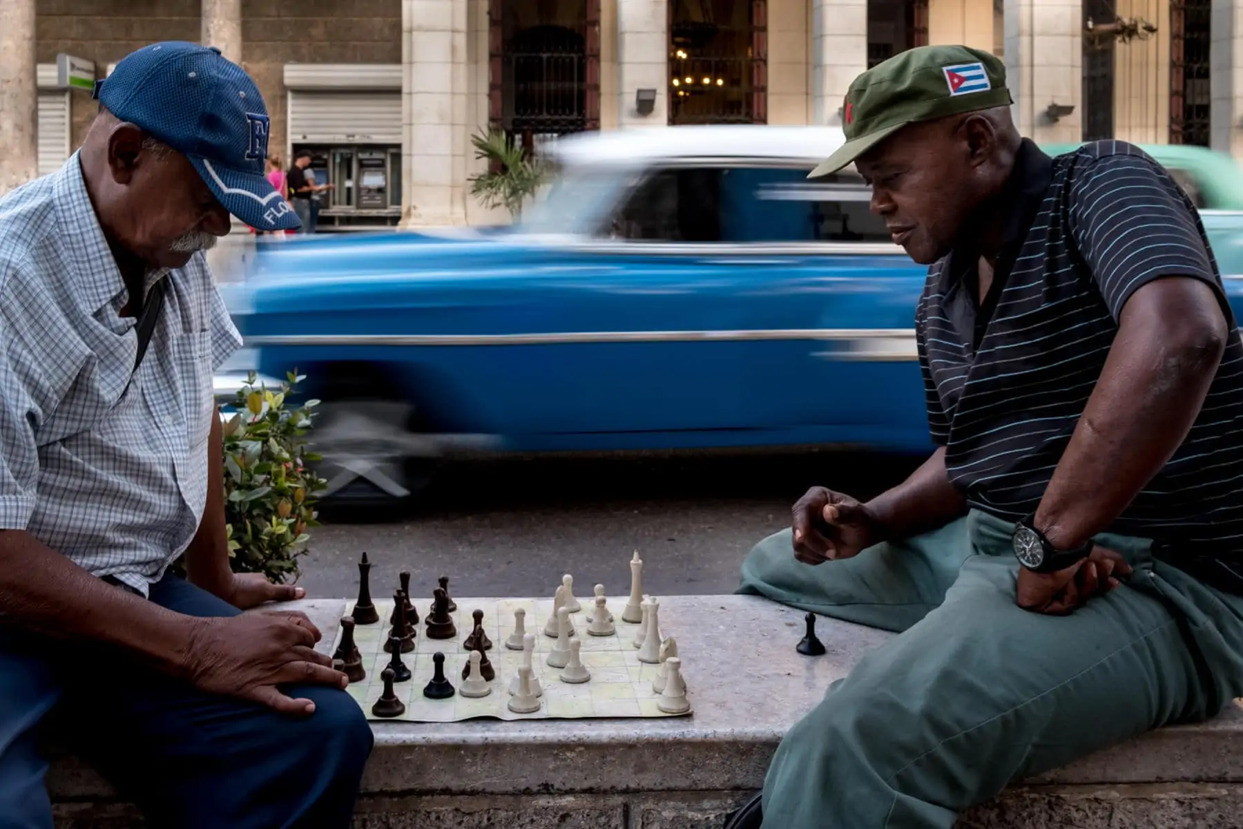 old men playing chess on the streets of Havana with blue Cuban car blurred in the background, taken by Havana street photographer Matt Badenoch