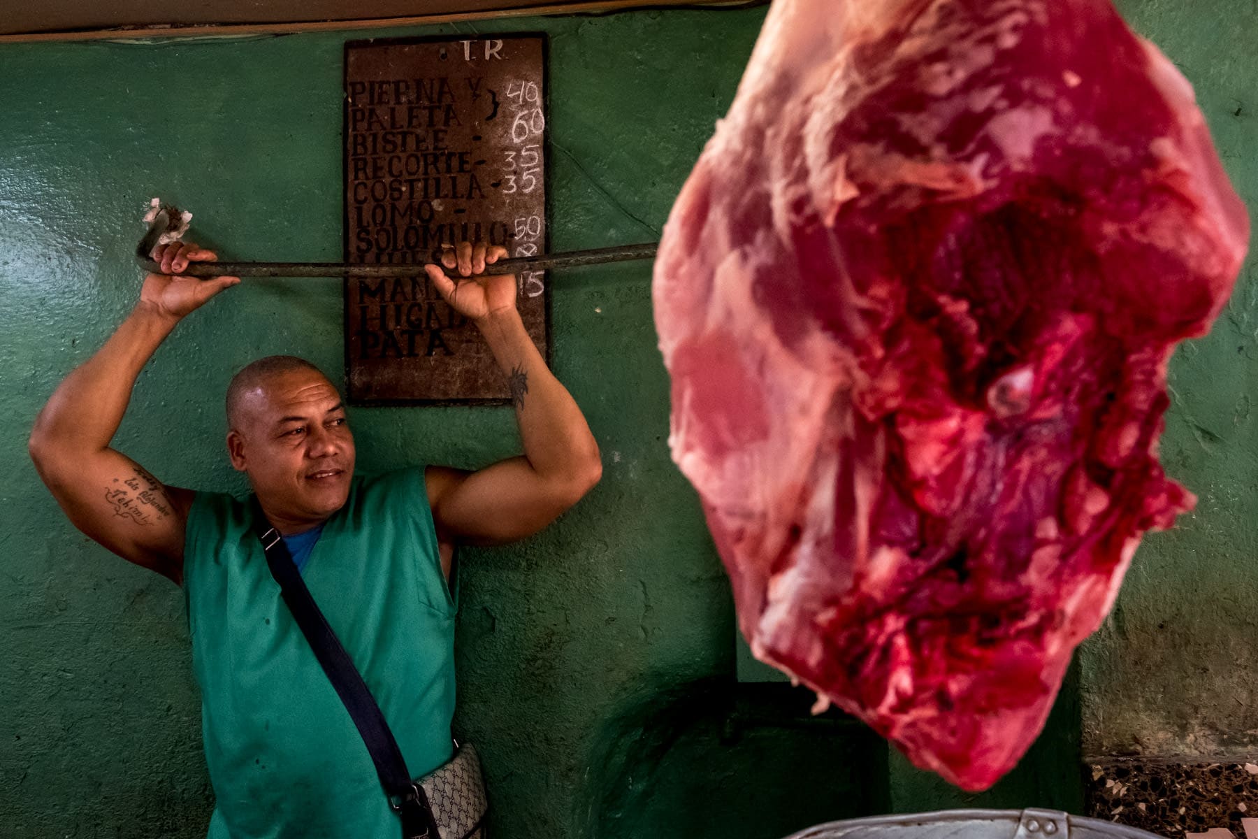 A man in green leaning agaist the wall at a meat market in Havana, Cuba