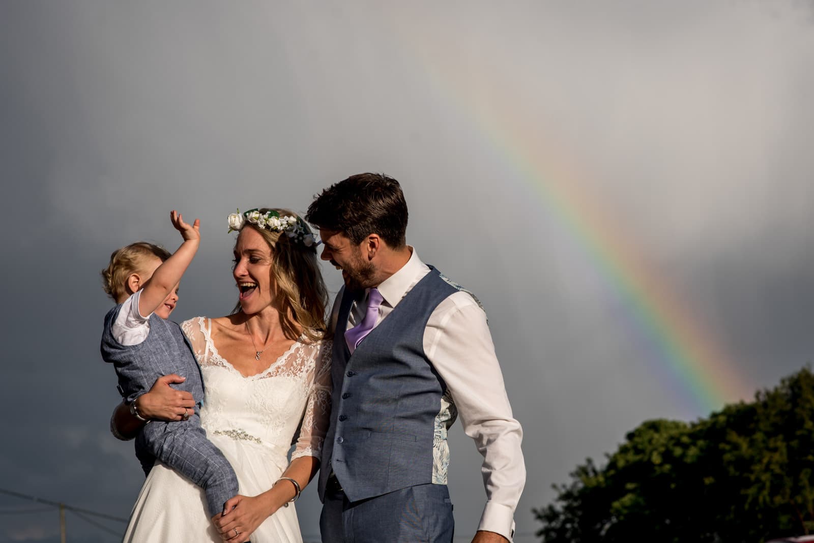 photo of bride and groom with their son in front of a rainbow on their wedding day