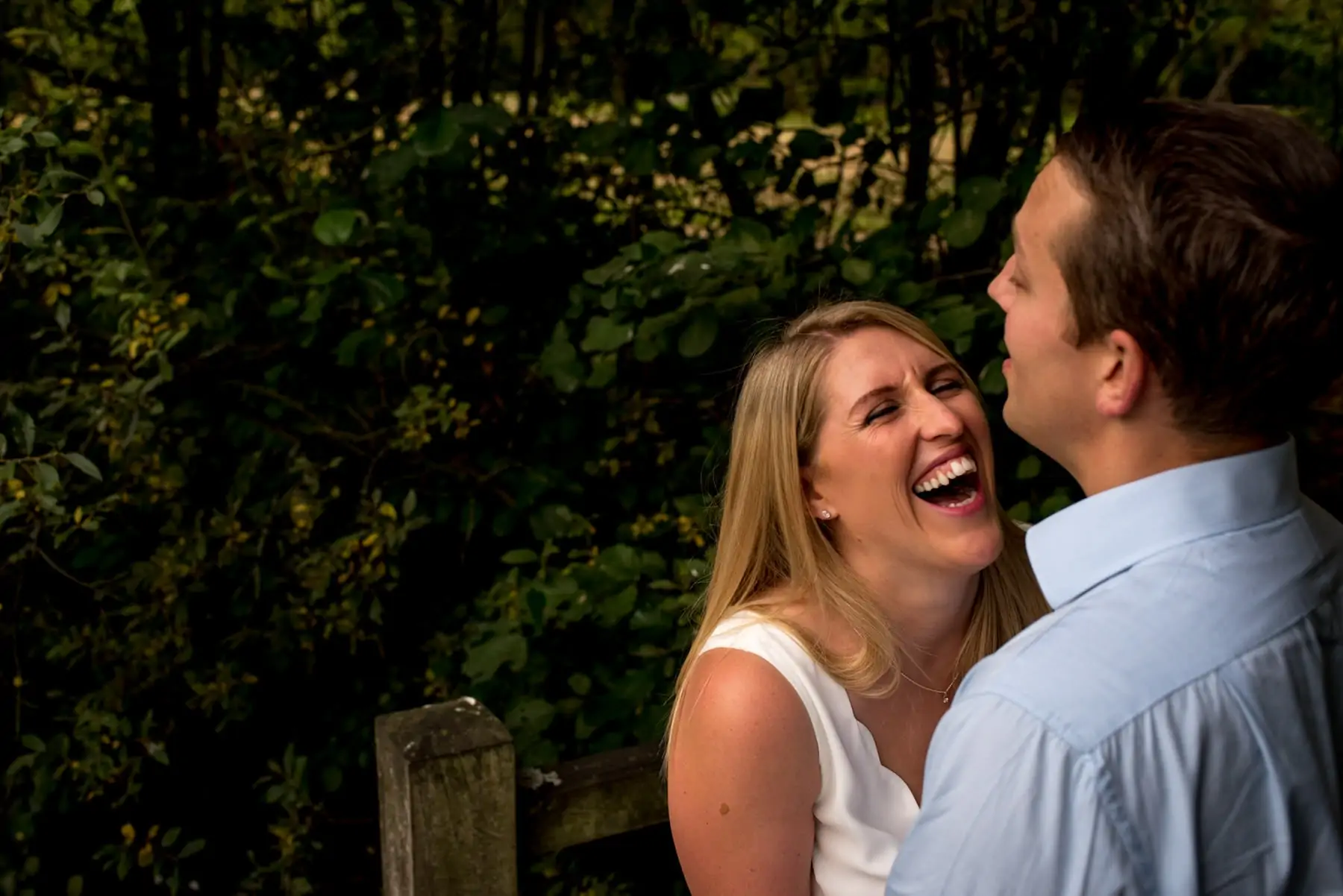 Photo of a women laughing really hard as her fiance hugs her in a park