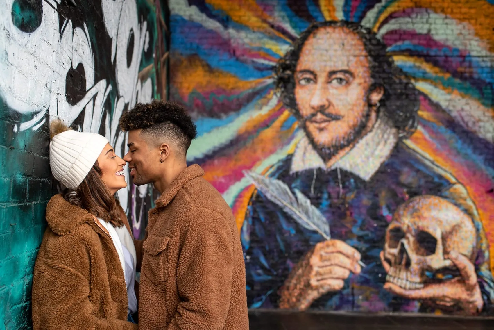 Photo of a recently engaged couple smiling in front of the colourful Shakespeare Graffiti next to Borough Market