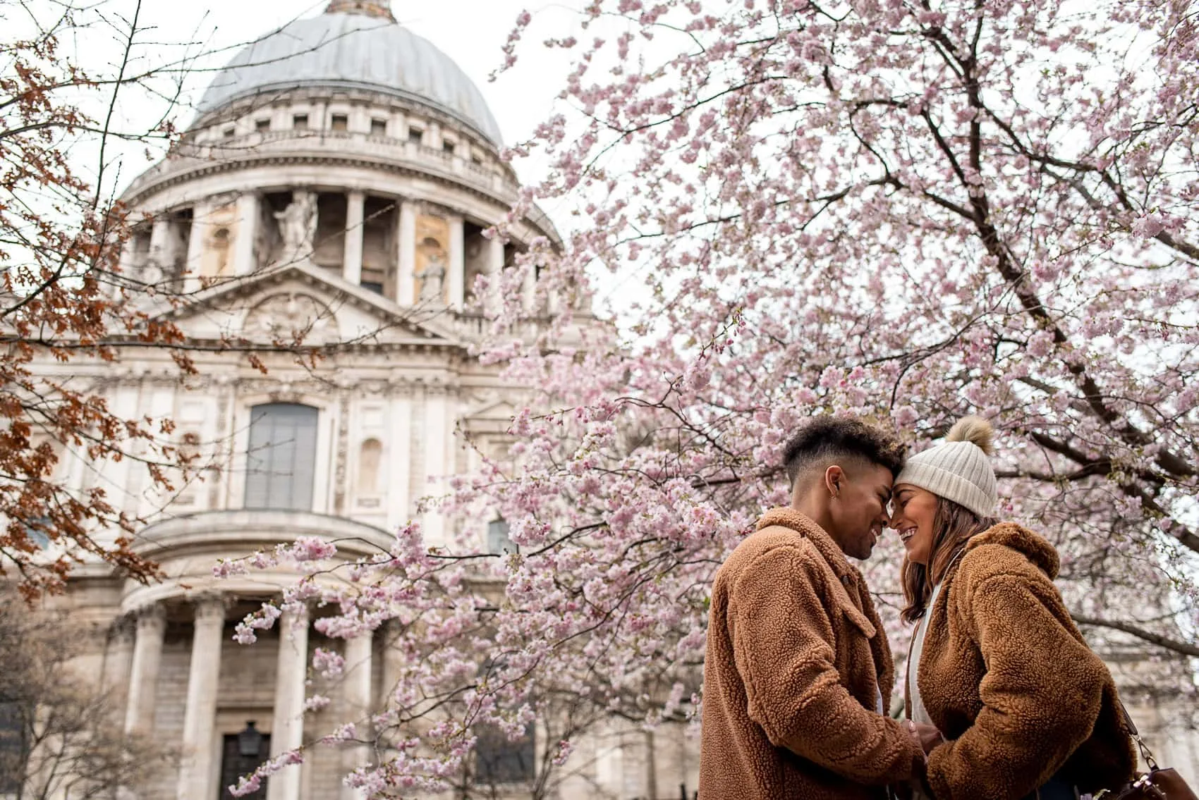 Photo of couple in front of St Pauls Cathedral with Cherry Blossoms in March during their engagement shoot
