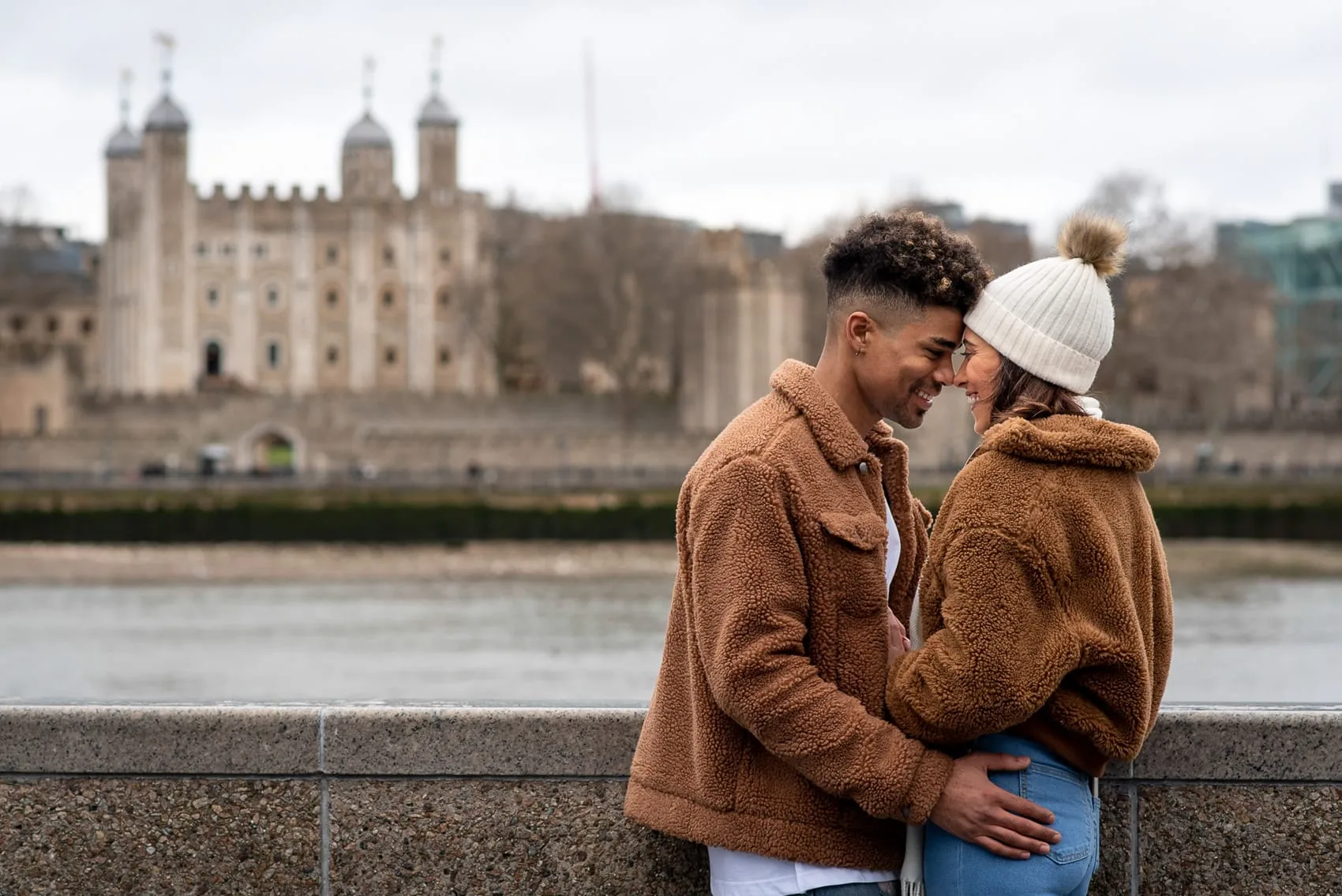 Engaged couple kissing and smiling in front of the Tower of London by the Thames