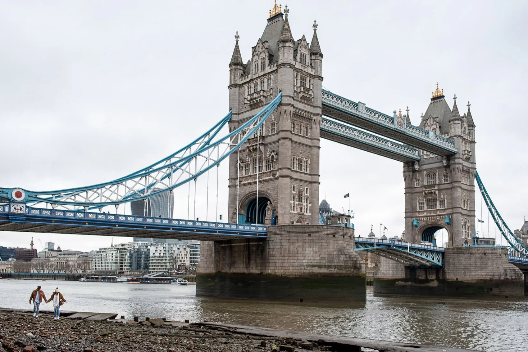 Couple walking on Thames Beach next to Tower Bridge at low tide in London