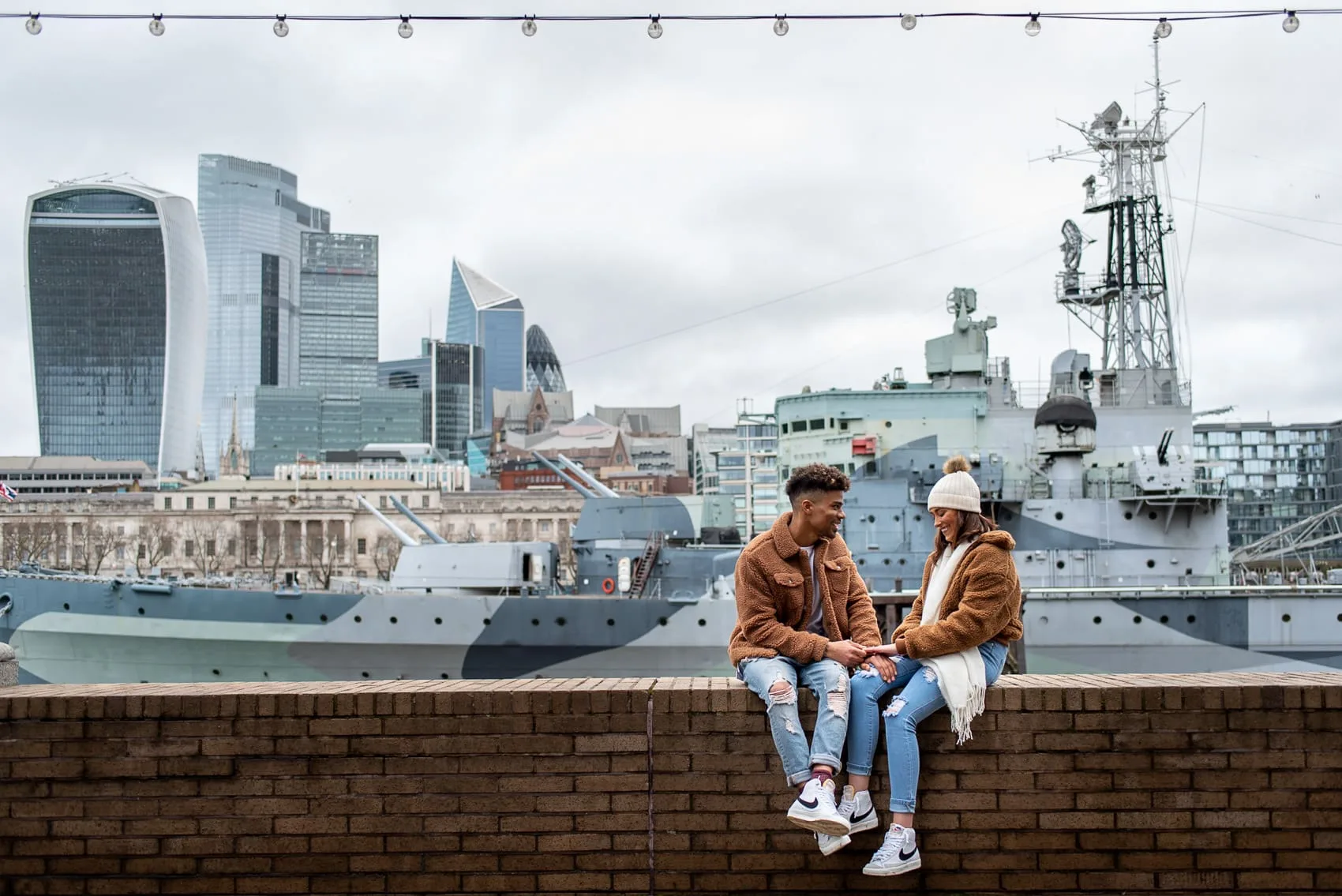 Couple sitting next to HMS Belfast and the city of London on their wedding proposal shoot