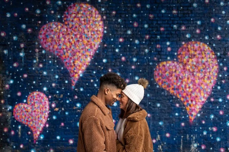 Photo of engaged couple in front of heart shaped graffiti in London