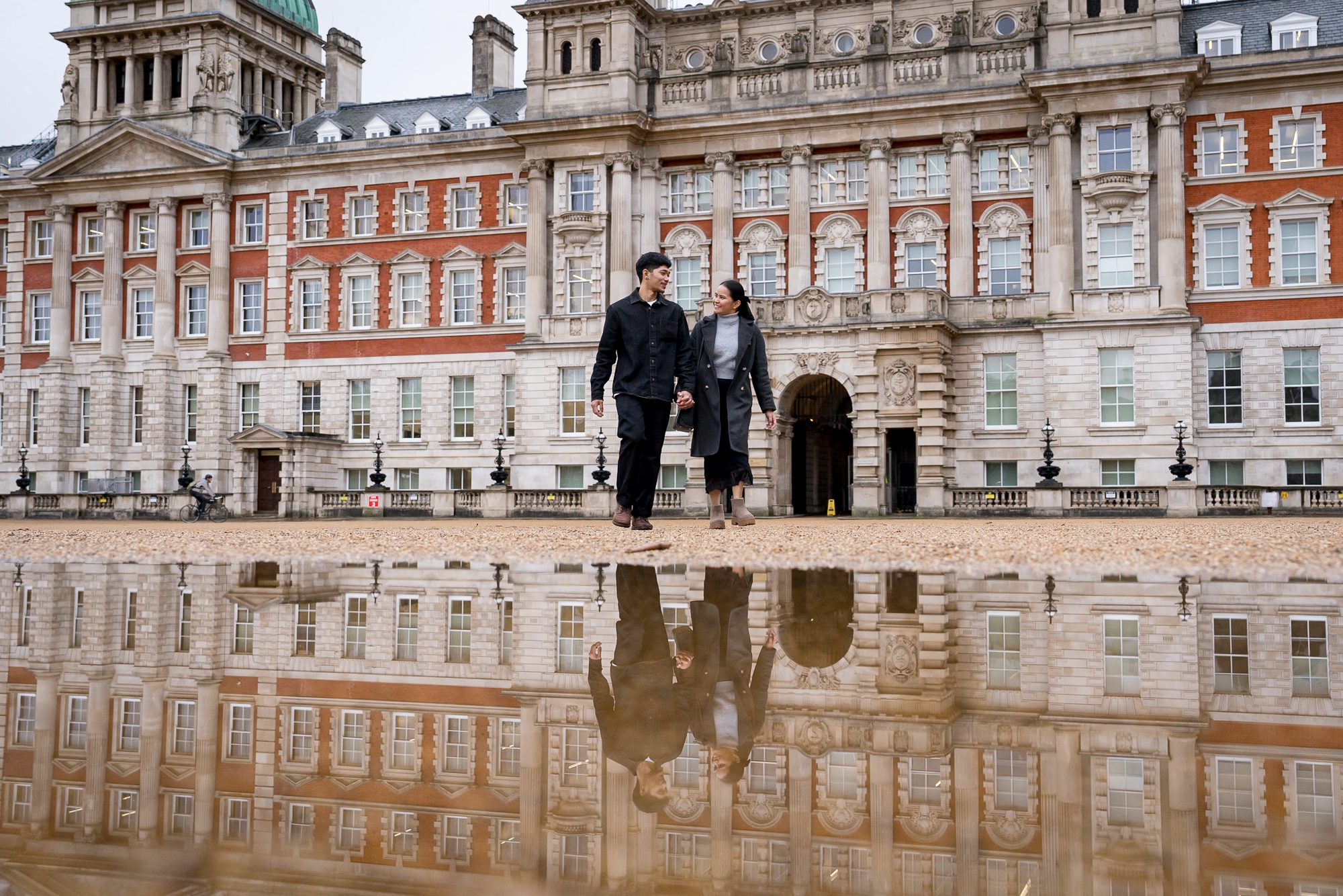 A couple walk across Horse Guards parade with their reflection in a puddle during their creative London proposal shoot