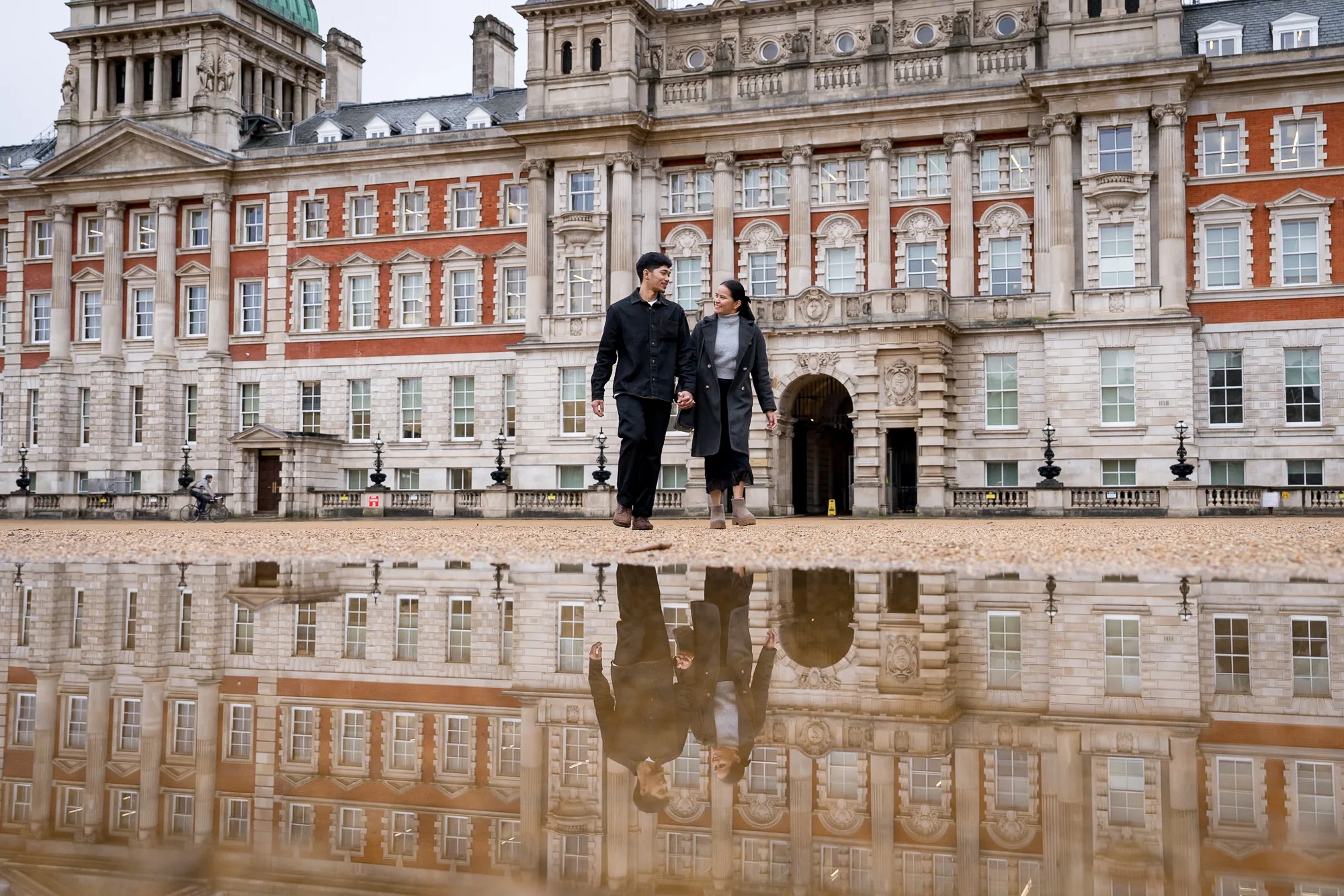 A couple walk across Horse Guards parade with their reflection in a puddle during their creative London proposal shoot