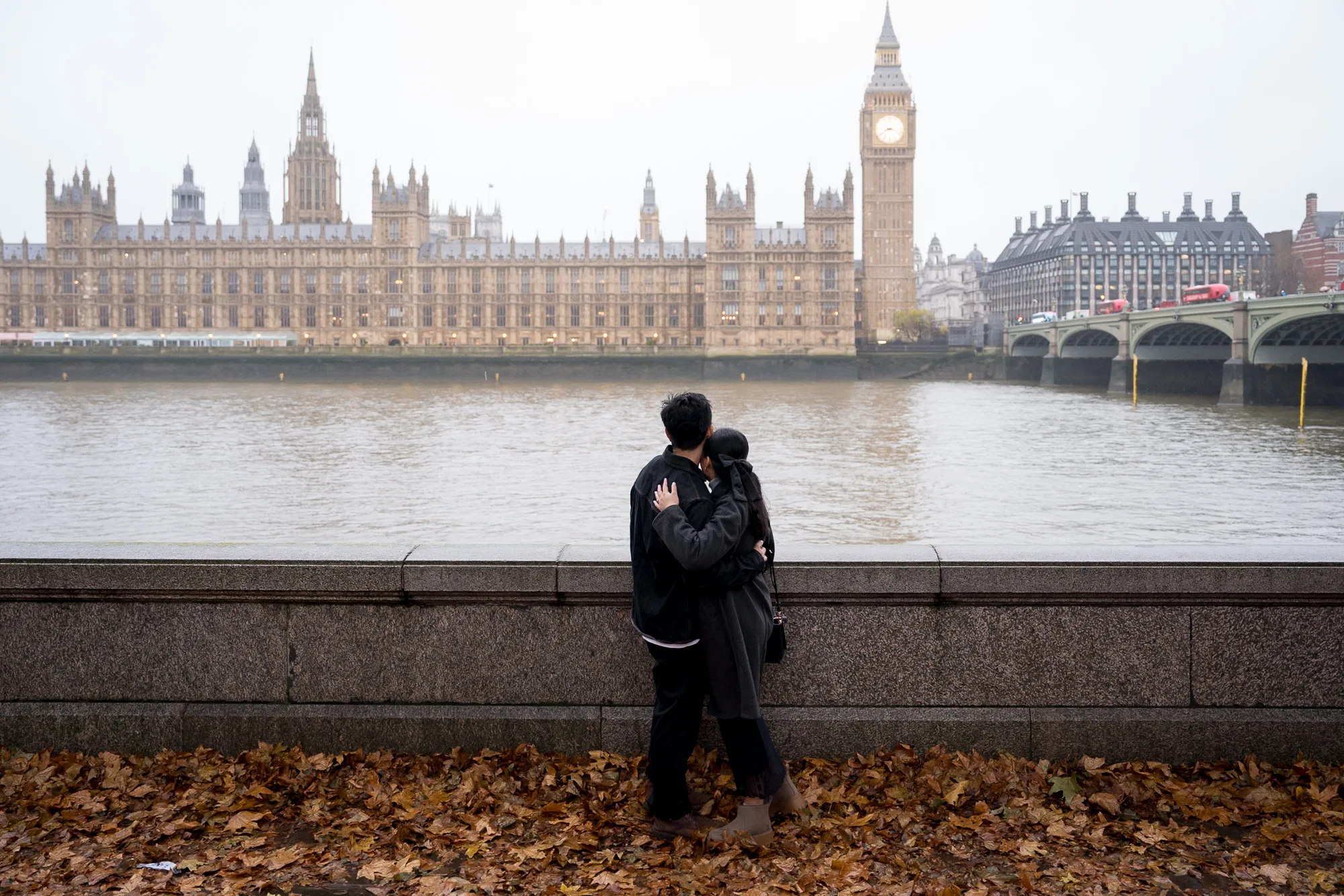 A couple hugging after getting engaged on a winter morning in London next to the Thames with Big Ben in the back ground