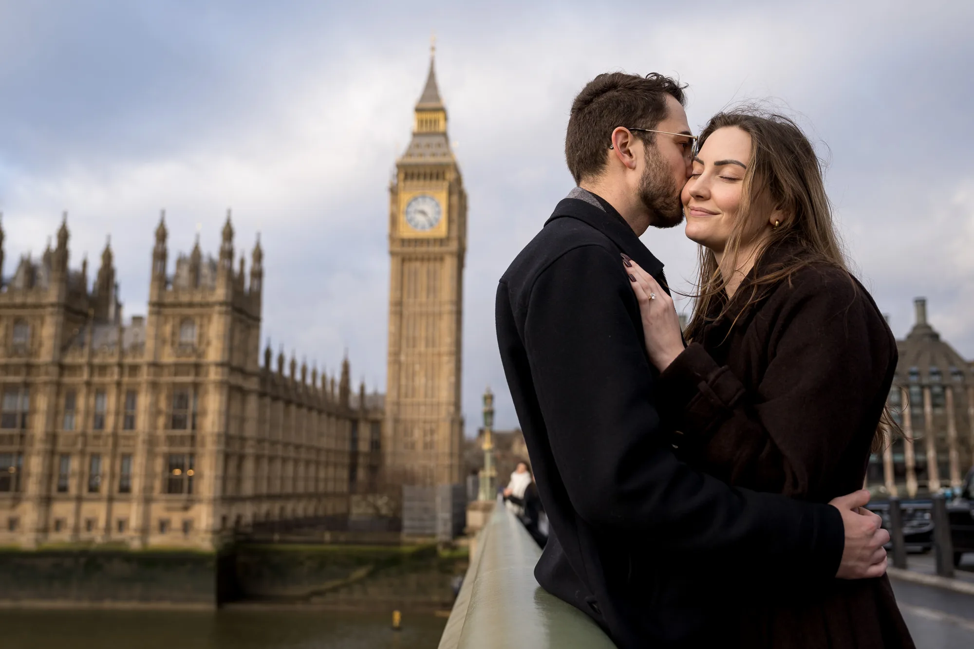 A couple. who just got engaged, embracing on Westminster Bridge with Big Ben and Parliament in the background.