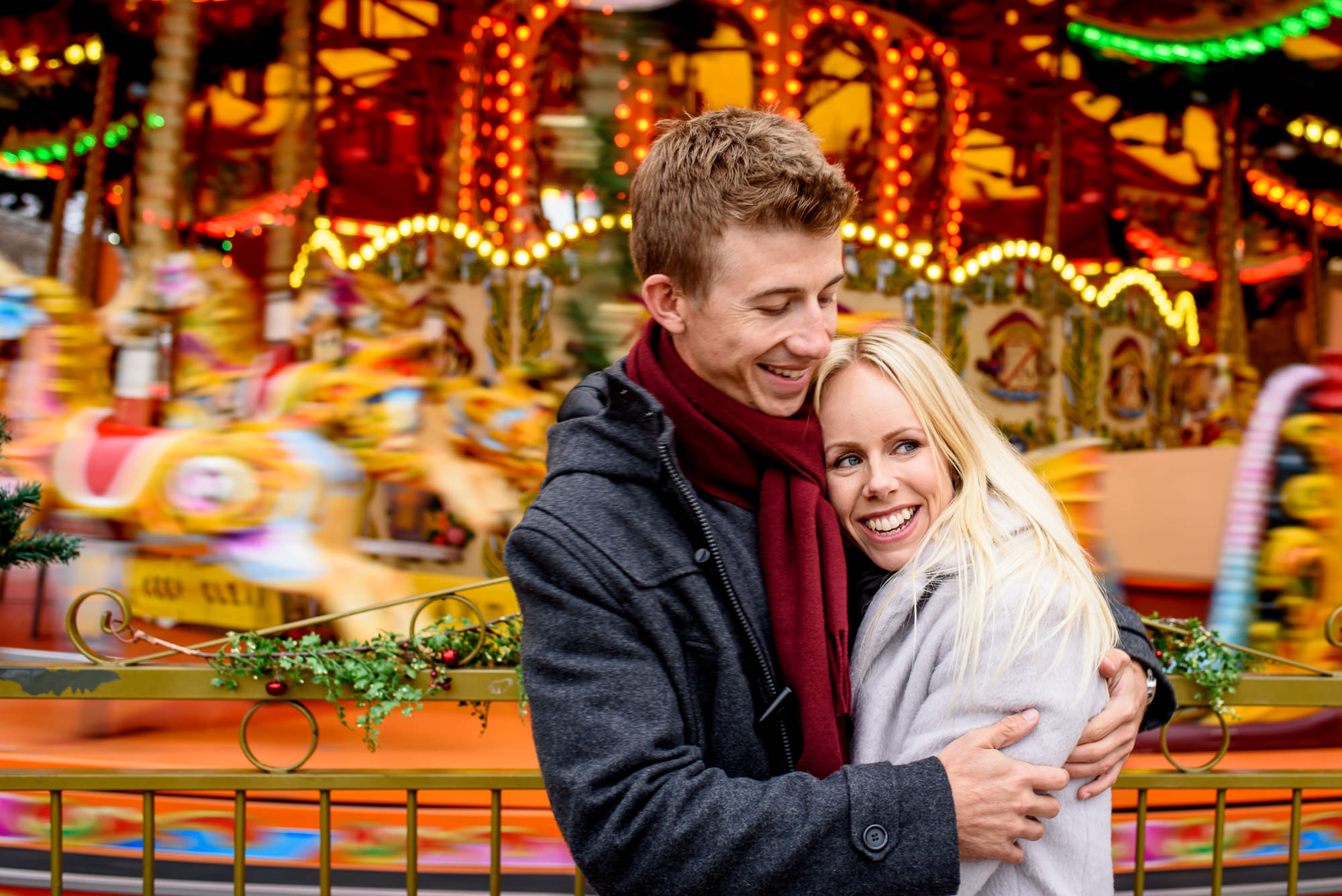 A couple hug and smile in front of a carousel at the Southbank Christmas market in London