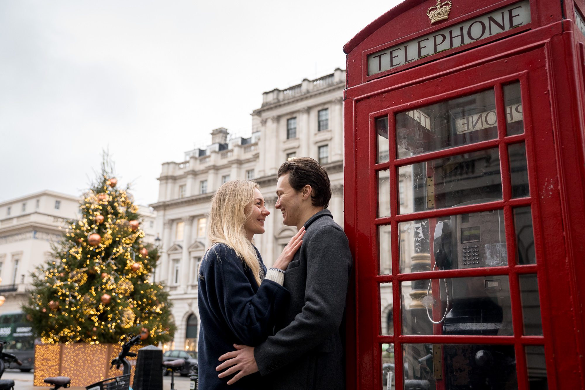 A couple enjoy a moment together leaning against a red London telephone box with a Christmas tree in the background