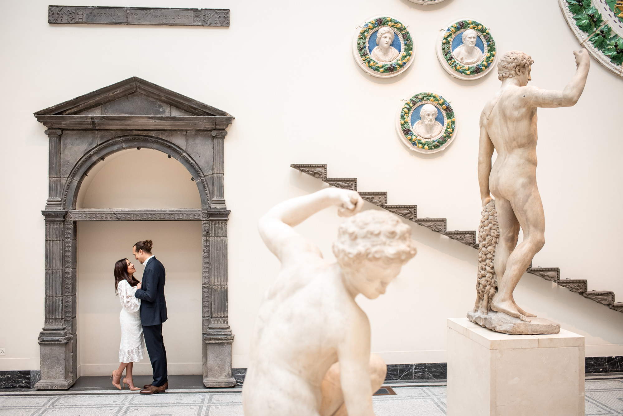 A couple surrounded by Roman statues and art during their engagement at the V&A museum in London