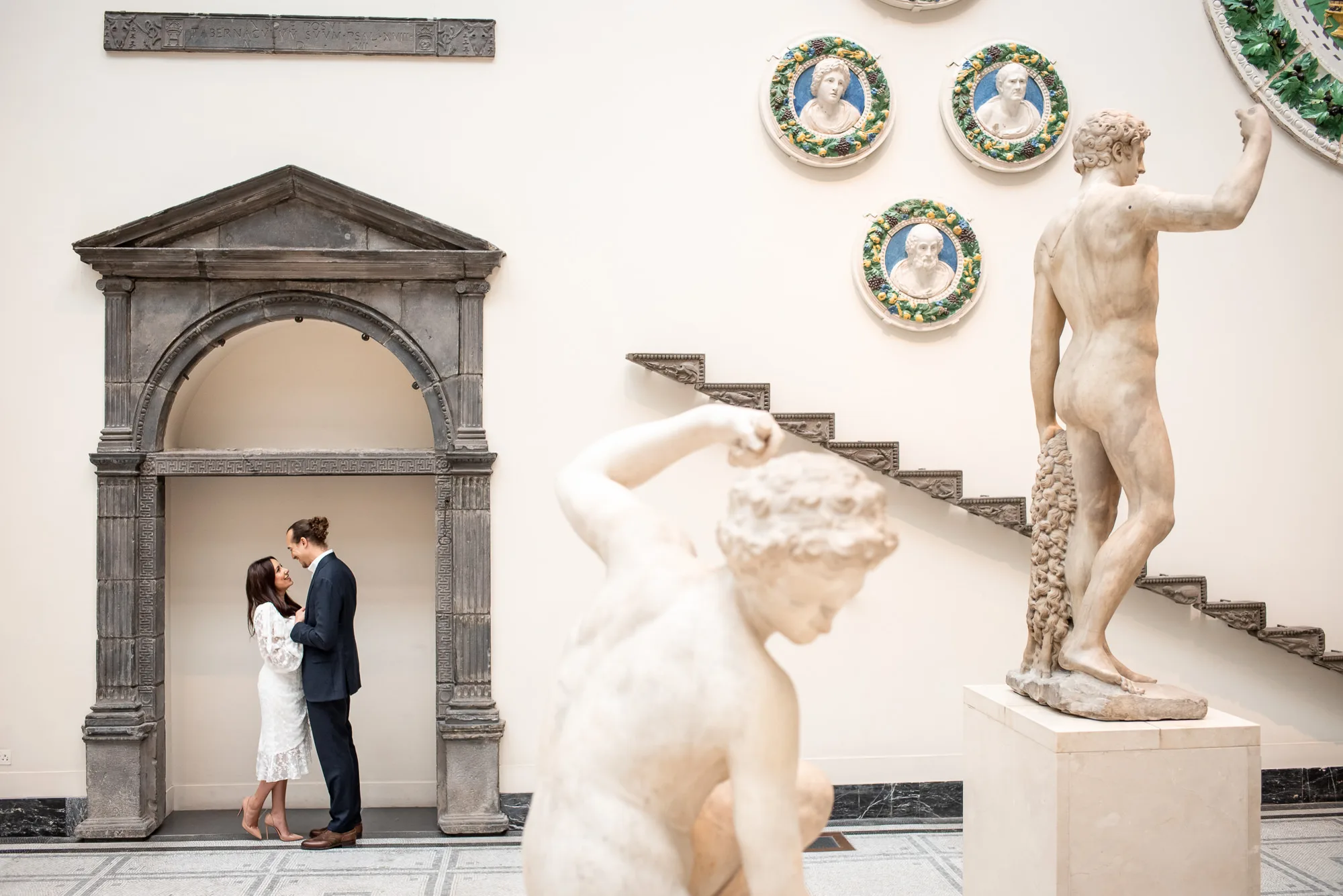A couple surrounded by Roman statues and art during their engagement at the V&A museum in London