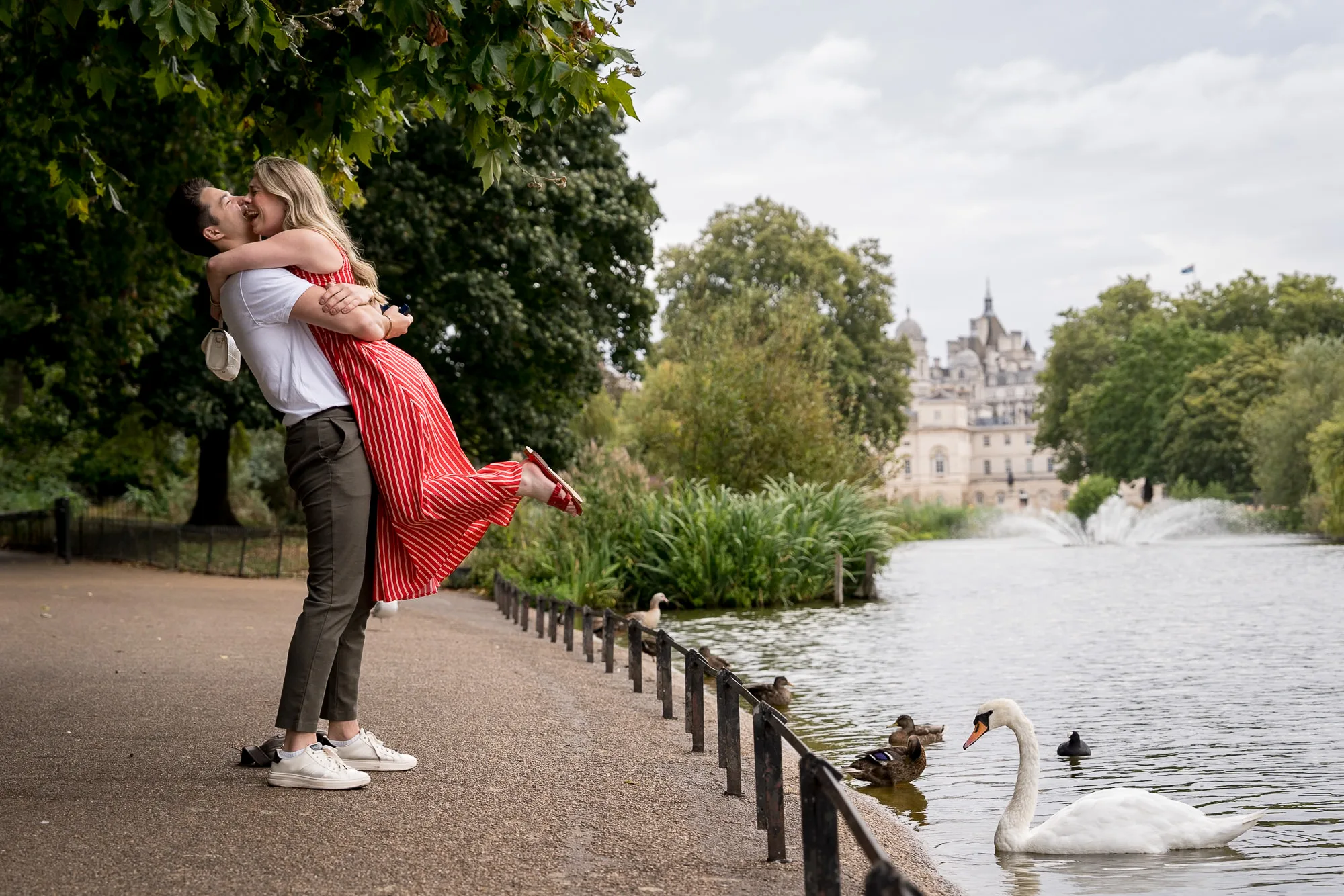 Boyfriend lifting up his new fiancé with big smiles who just said yes to his proposal. Swan and pond in the background, taken in St James Park.