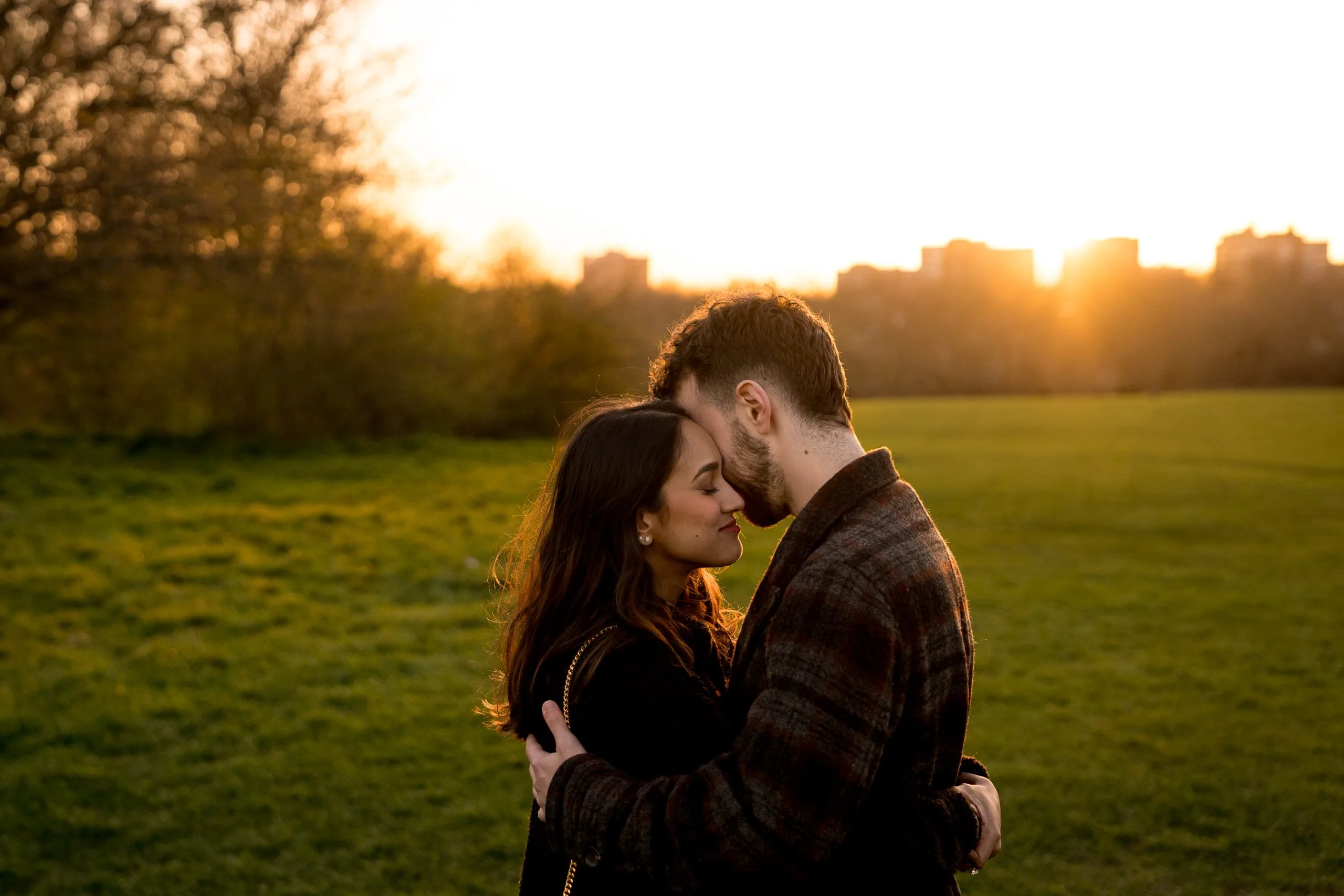 A newly engaged couple embracing at sunset in Primrose Hill Park in London
