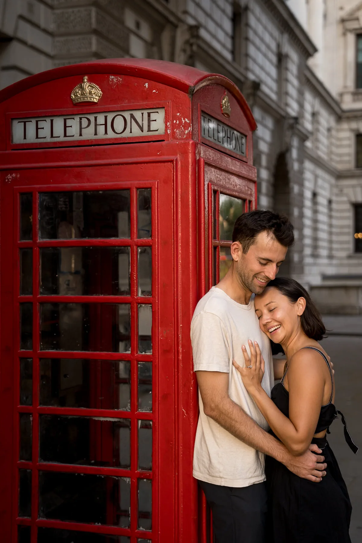 A couple embrace against a Red Telephone Box in Westminster, London, after he proposed to her. They are both smiling and the engagement ring is on show on her finger