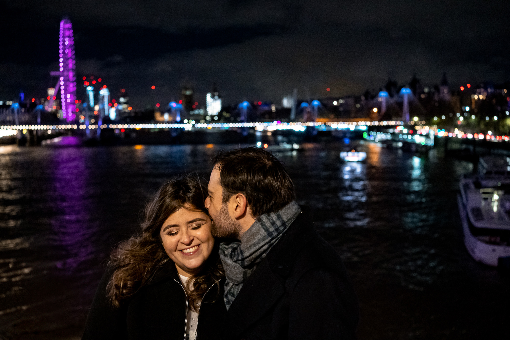 A couple celebrating their proposal at night with the London Skyline (London Eye) and river thames in the background