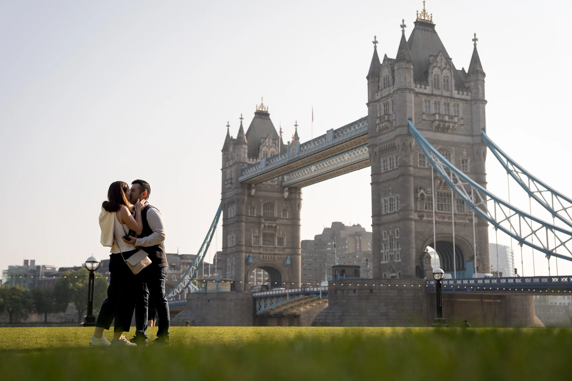 A couple kissing in front of Tower Bridge moments after he proposed to her on a summer's morning in London