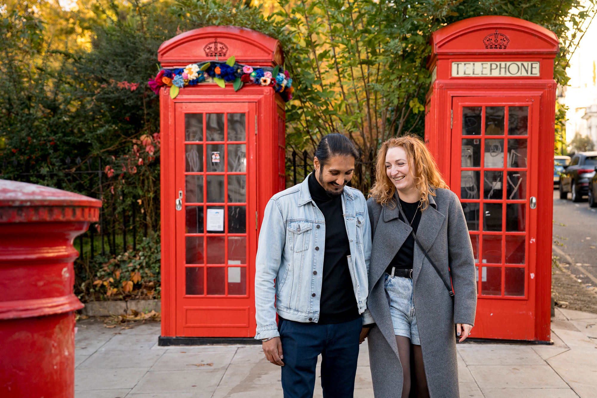 A recently engaged couple laughing in front of some London red telephone boxes in Primrose Hill