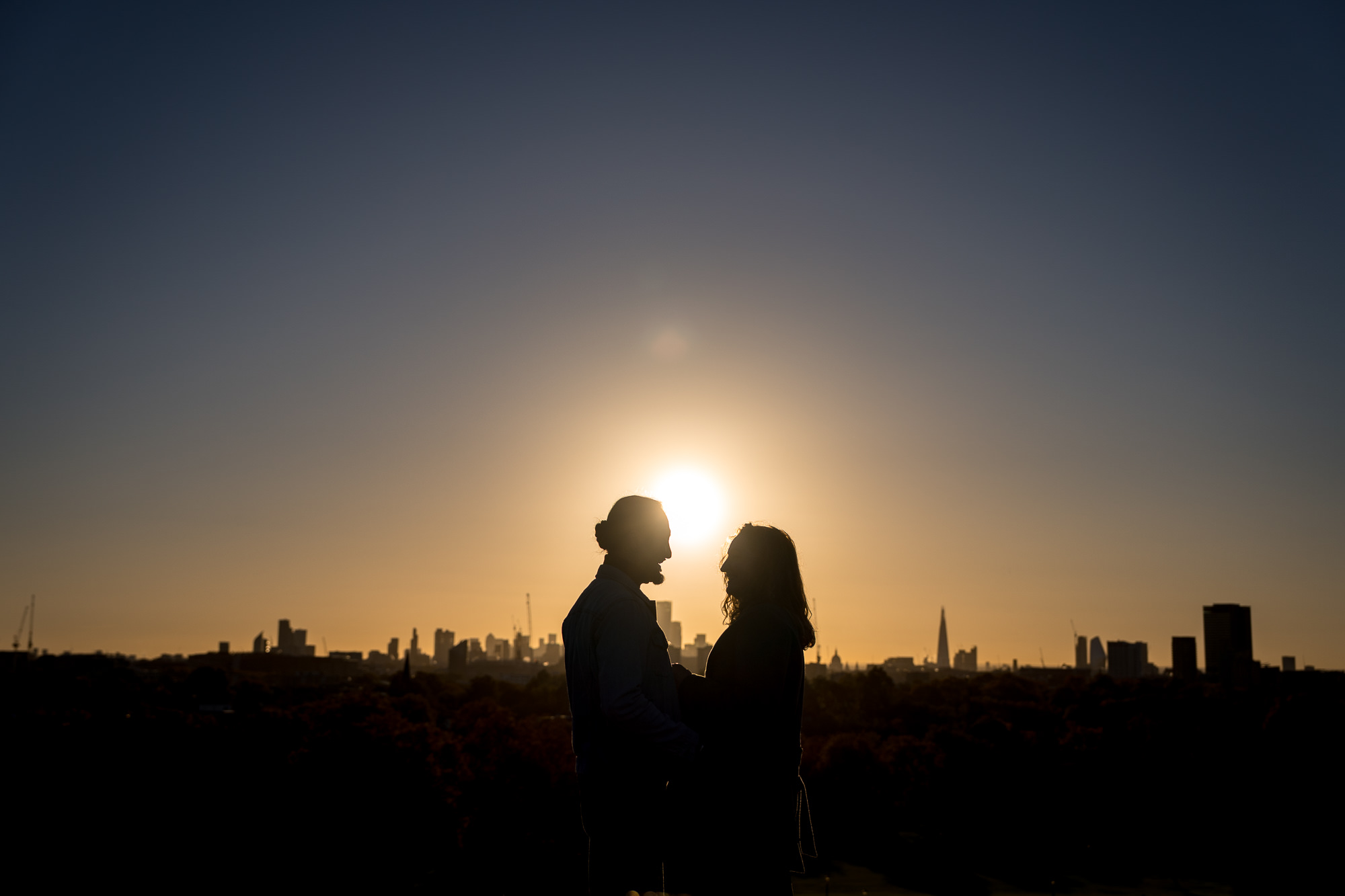 A silhouette photo at sunrise of a couple with the London skyline in the background