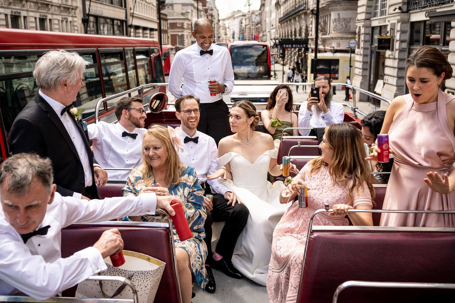 A wedding party on the top of an open roof double decker bus in London, enjoying drinks and the city