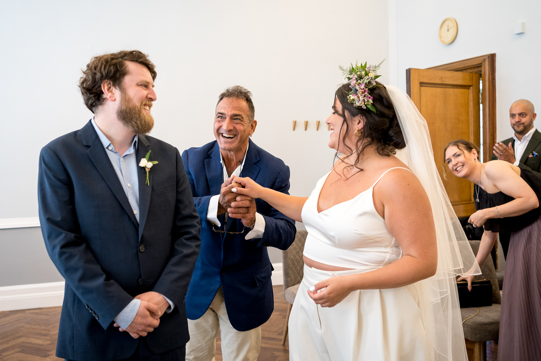 Father giving his daughter away to her husband, while laughing at their wedding in the Islington Town Hall