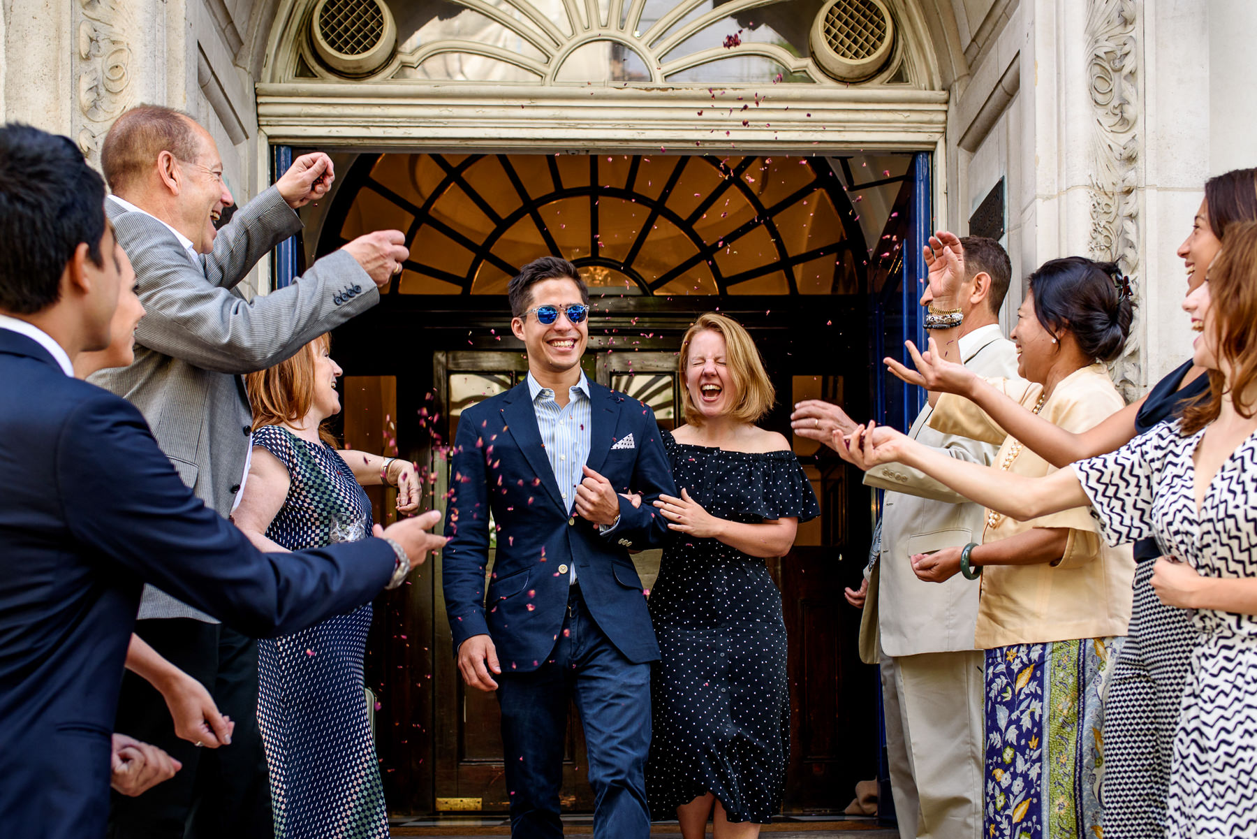 A couple walking out of Chelsea Old Town Hall with confetti and guests cheering their marriage